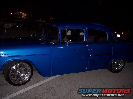 Blue sedan with chrome wheels, side view. Appears to be a 1955 Chevrolet