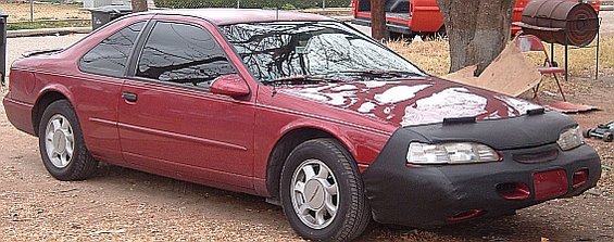 Red 1994 Ford Thunderbird coupe with a black car bra and peeling hood paint