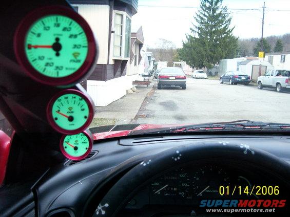 Dashboard with three glowing green gauges, looking out at a street with cars and houses