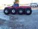 1979 Ford Bronco - A red pickup truck is modified with six enormous tires, parked next to a white van.