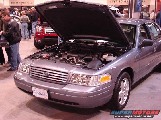 Gray 2000 Ford Crown Victoria at an auto show, hood open showing engine