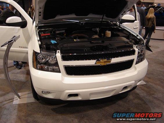 Front view of a white Chevrolet SUV, hood open, showing the engine bay. The Chevrolet logo is prominent on the grille