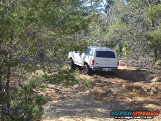 White SUV on a dirt path, rear view. Tires are kicking up dust