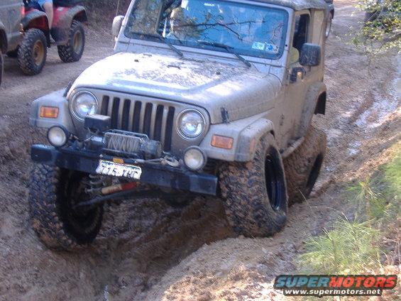 Muddy Jeep Wrangler driving through a ditch with another ATV behind it