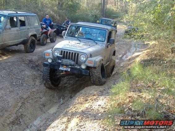 Tan Jeep Wrangler with winch on muddy trail, front view