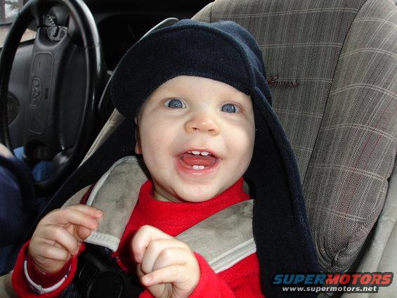 Baby wearing a hat in a car seat, looking at the camera