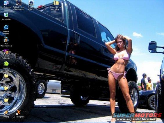 Woman in pink bikini poses next to a black lifted pickup truck; other vehicles and people in background
