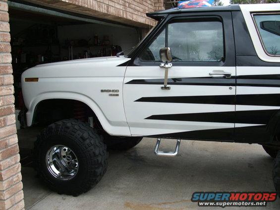 White and black 1985 Ford Bronco with large tires and custom graphics