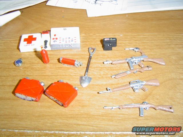 Toy guns, gas cans, first aid kit, and shovel on a wooden surface