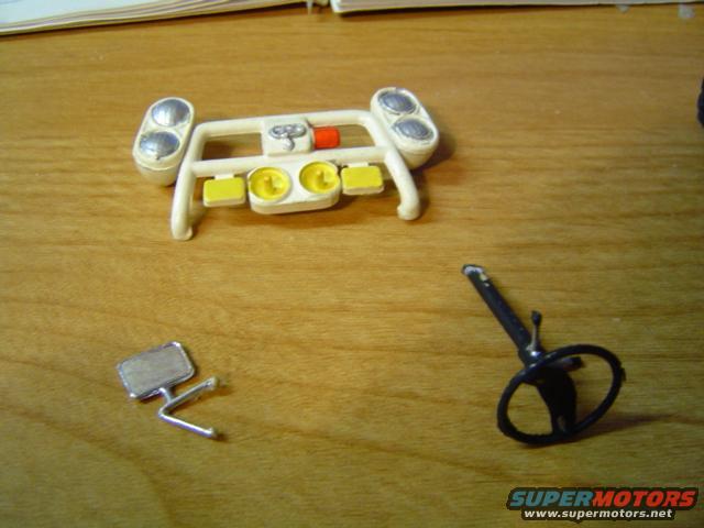 Model car dashboard, steering wheel, and side mirror parts on wooden surface