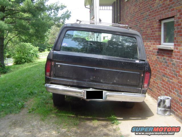 Rear view of a black 1978 Ford Bronco parked on gravel next to a brick house