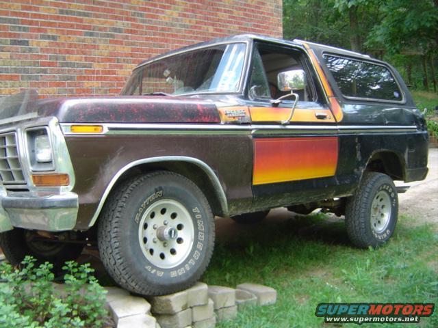 Side view of a brown and black Ford Bronco with orange and yellow graphics on the side. It's parked on some bricks