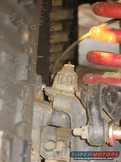Close-up of dirty suspension parts, including a tire, red coil spring, and metal linkage