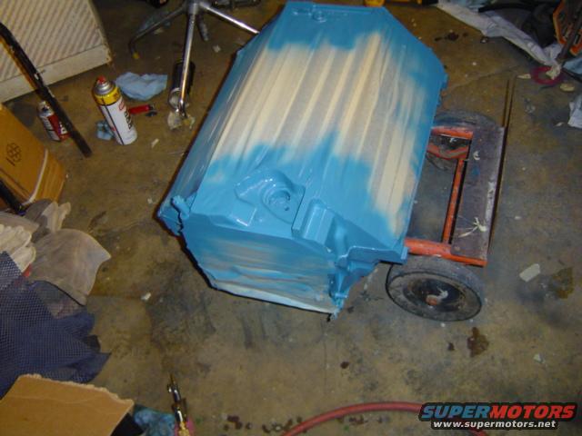 Engine block painted blue and tan, resting on an orange dolly with two wheels