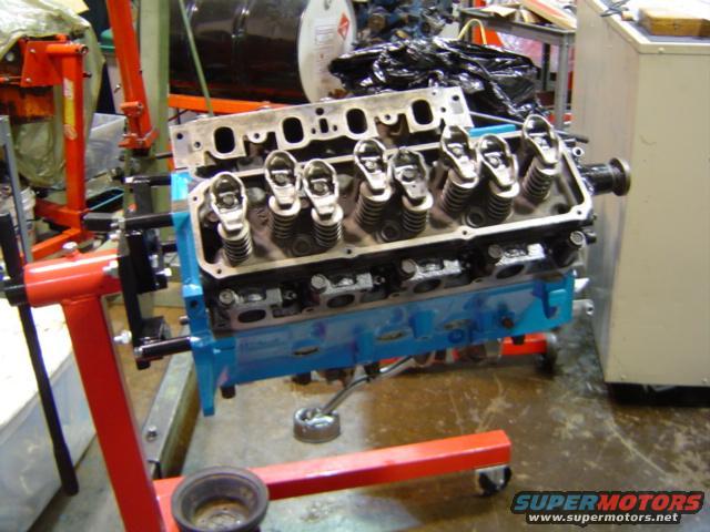 Blue engine block with cylinder head on an engine stand, showing valve train components