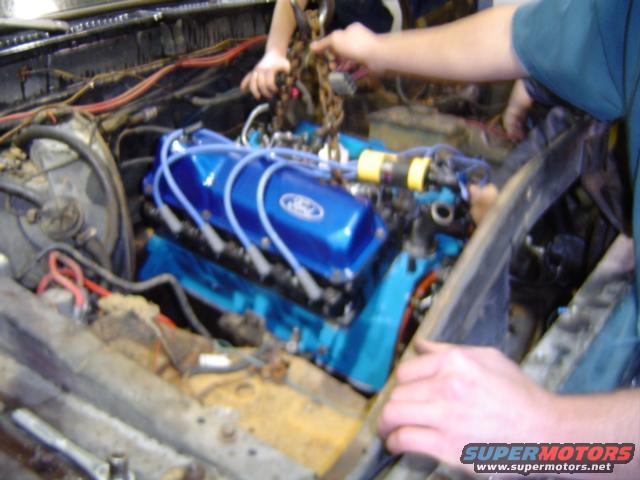 Blue Ford engine being installed with spark plug wires and valve covers
