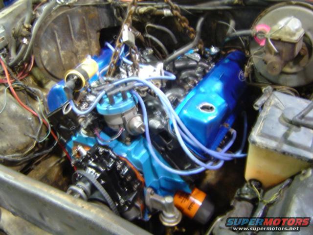 Engine with blue valve covers and distributor cap being worked on, with chains attached