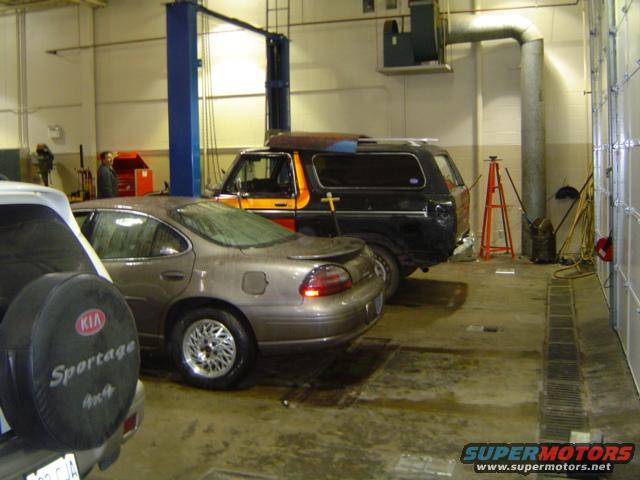 Black Ford Bronco with orange stripe, parked in a garage next to a sedan. A Kia Sportage is partially visible in the foreground