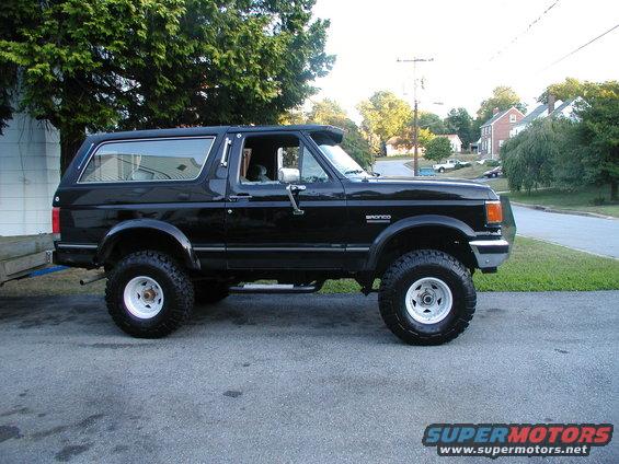 Black 1990 Ford Bronco lifted with white wheels, side view
