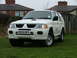 2006 Mitsubishi L200 - This white SUV, identified by its license plate BX55 MFV, features a distinctive hood scoop and is parked on a grassy lawn.