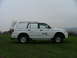 2006 Mitsubishi L200 - A white van with BT branding is parked on a grassy hill under an overcast sky.