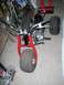 1900 Honda Big Red - A red three-wheeler ATV with knobby tires and chrome handlebars is parked indoors.