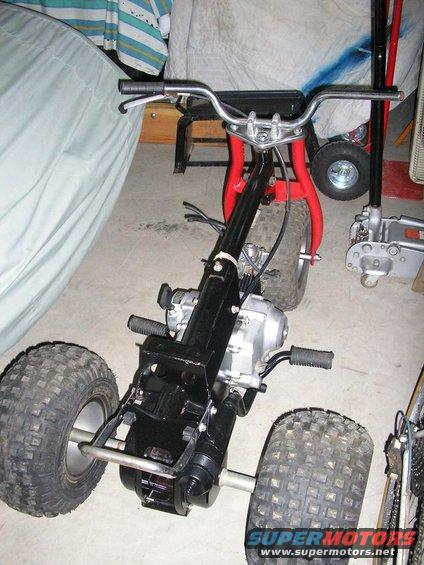 Three-wheeled ATV with black frame and red front forks, knobby tires, and handlebars