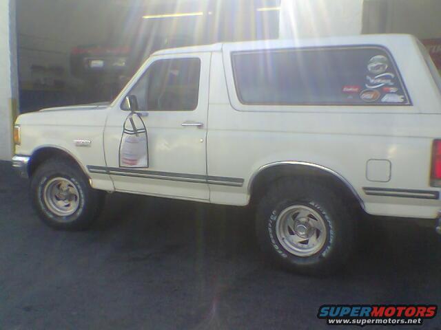 side view of a white SUV with stickers on the rear window and a bag hanging from the driver's door