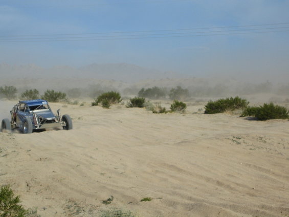 Blue off-road buggy driving on sand, kicking up dust