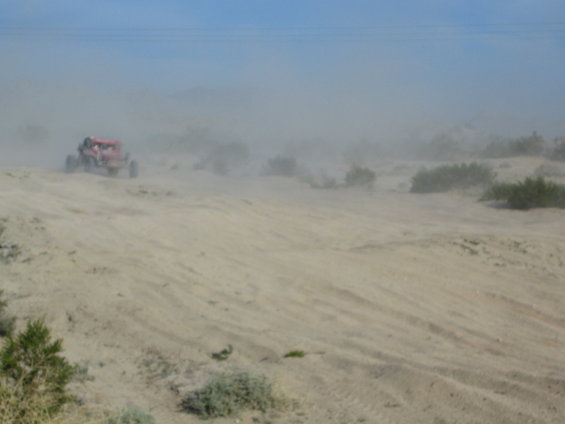 Red dune buggy kicking up dust on a sandy hill