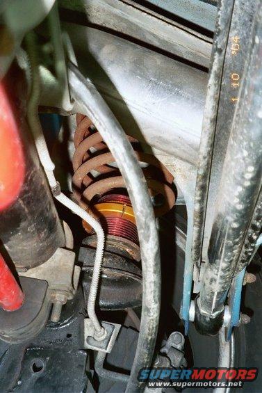 Close-up of rusty coilover shock absorber with red and yellow bands, part of a vehicle's suspension