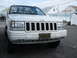 1997 Jeep Grand Cherokee - A white Jeep Grand Cherokee is parked outside with houses in the background. The license plate is visible.