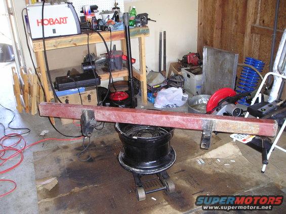 Red metal bumper on a black jack with a tire underneath, in a garage with tools and a welder