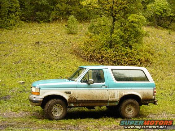 1995 Ford Bronco parked on a muddy, grassy hill with trees in the background