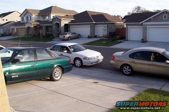 Green sedan, white sedan, and tan sedan parked in front of suburban houses