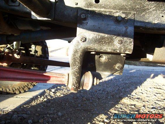 close-up of a vehicle's suspension bracket and linkage, with a tire visible in the background