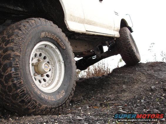 Truck tire on dirt mound, showing Pro Comp Mud Terrain tire and part of white body