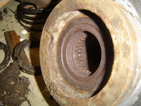 Rusted axle hub with internal splines and surrounding corroded metal. Disassembled parts and dirt are visible