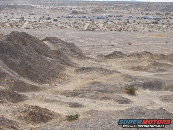 Desert terrain with hills and a group of RVs and cars in the background