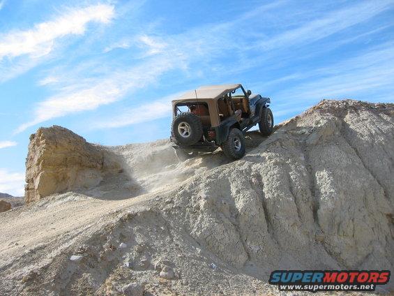 Jeep Wrangler climbing a steep dirt hill, kicking up dust