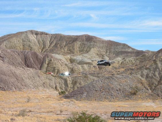 Two SUVs driving on rocky desert terrain under a blue sky