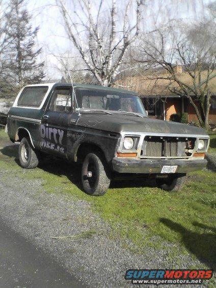 1978 Ford Bronco with "Dirty Deeds" painted on the side, parked on gravel and grass