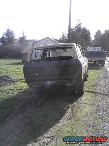 1978 Ford Bronco, rear view, dark color, dented rear bumper, parked on dirt road