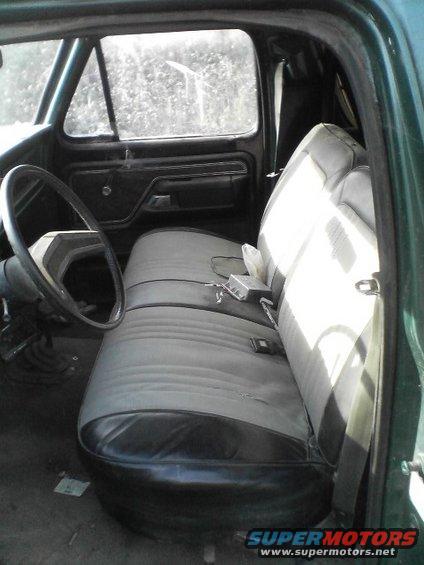 Green vehicle interior with grey bench seat, black dashboard, and steering wheel