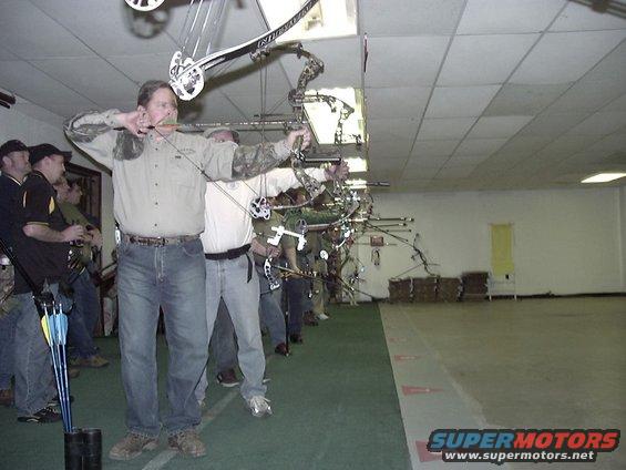 People practicing archery indoors, aiming bows at targets down a range