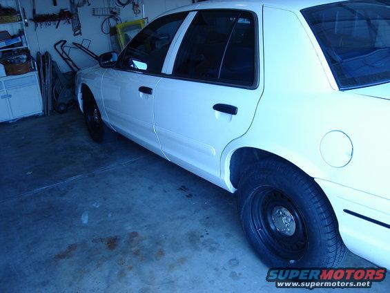 White sedan parked in a garage, side view. Black steel wheels and tinted windows are visible
