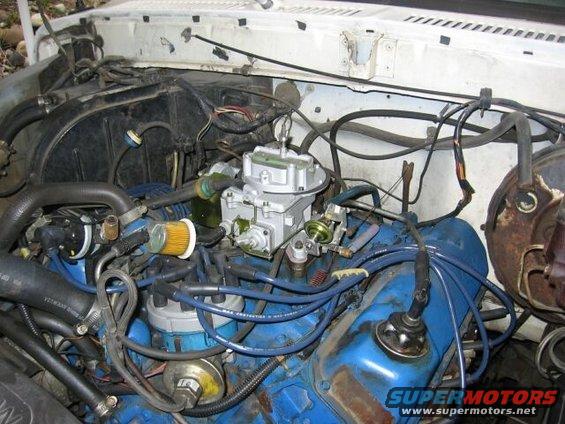 Engine bay of a 1979 Ford Bronco with a blue engine block, carburetor, and spark plug wires