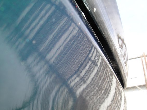 Dark blue car body panel gap with reflections of a fence