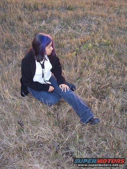 Person with blue-streaked hair sits in dry grass, looking away