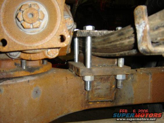 Close-up of a rusty leaf spring attached to a differential housing with bolts and metal plates